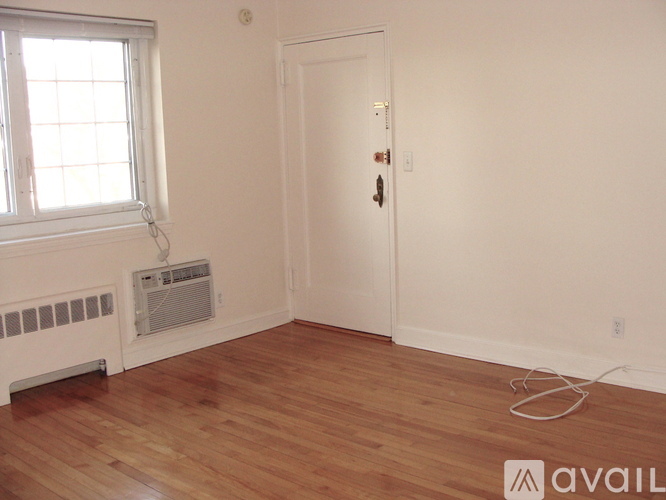 A room with a white door, a window with blinds, and a radiator under the window.