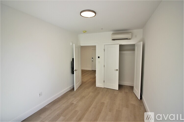 A room with a white wall and a wooden floor with a white door and a white cabinet.