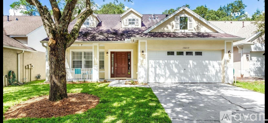 A white house with a brown door and a tree in front.