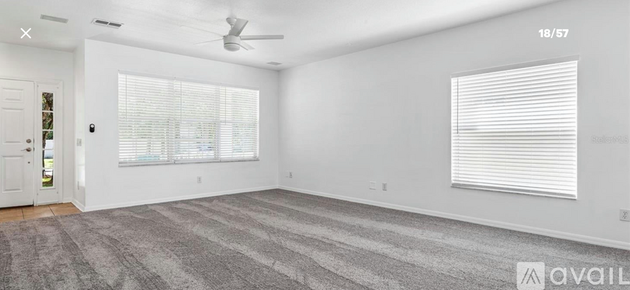 A spacious room with a carpeted floor, a ceiling fan, and a window with blinds.