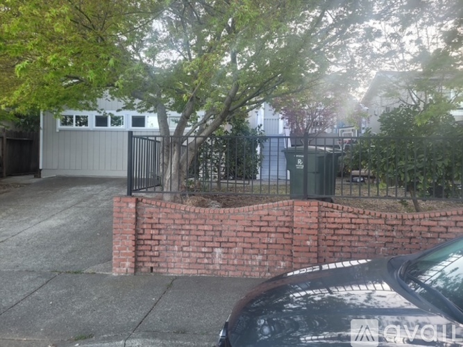 A black car is parked in front of a brick wall and a tree.