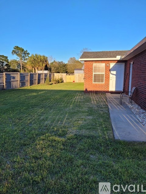 A house with a white door and a brick wall is surrounded by a grassy area and a fence.