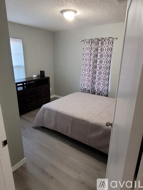 A bedroom with a bed, dresser, and window with curtains.