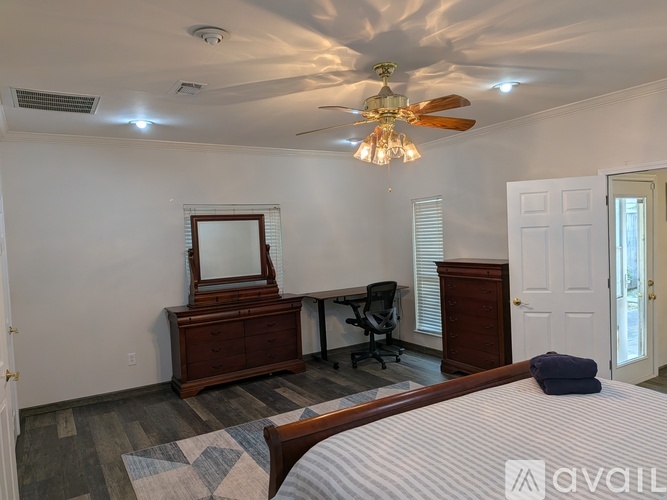 A bedroom with a bed, desk, chair, and a ceiling fan.