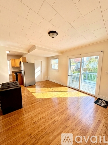 A spacious room with wooden floors and a kitchen area with a refrigerator and cabinets.