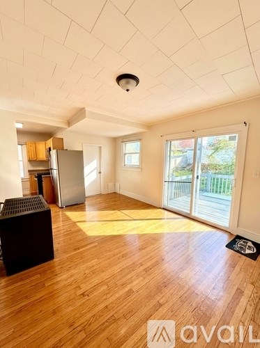 A spacious room with wooden floors and a kitchen area with a refrigerator and cabinets.