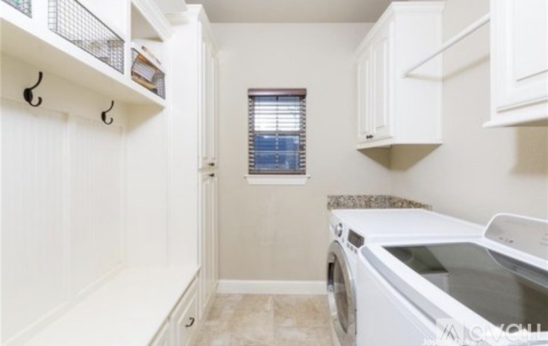 A white washing machine is in a laundry room with white cabinets and a window.