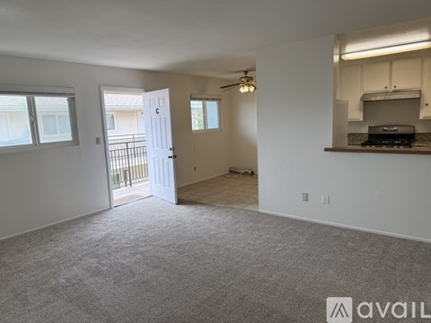 A spacious living room with a carpeted floor and a kitchen area with a stove top oven.