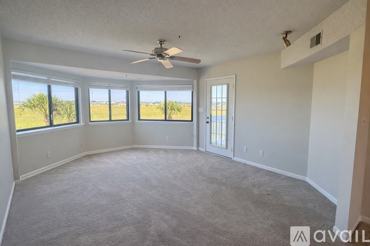 A spacious room with a ceiling fan and large windows overlooking a grassy area.