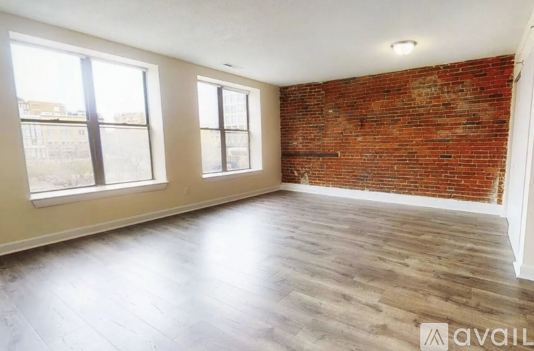 A room with a red brick wall and wooden flooring is available for rent.