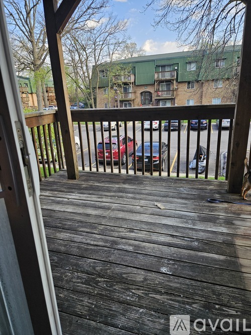 A wooden deck with a railing and a view of a parking lot and buildings in the background.