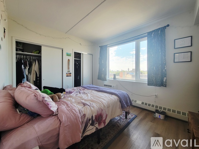A bedroom with a bed covered in pink bedding and a window with blue curtains.