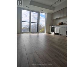 A large empty room with wooden floors and a kitchen area in the background.