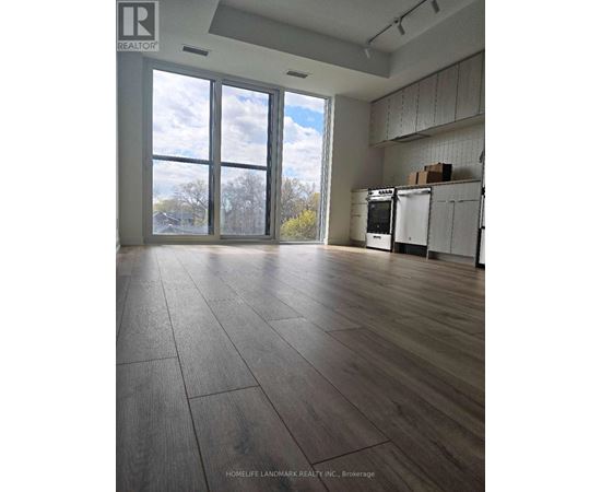 A large empty room with wooden floors and a kitchen area in the background.
