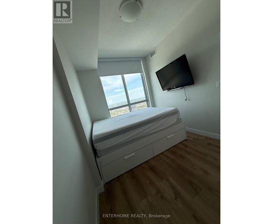 A bedroom with a bed, a window, and a flat screen TV mounted on the wall.