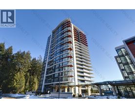 A tall residential building with balconies is surrounded by trees and has a clear blue sky in the background.