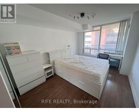 A bedroom with a bed, nightstand, and a window with a view of a building outside.