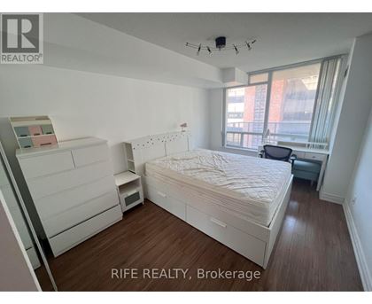 A bedroom with a bed, nightstand, and a window with a view of a building outside.