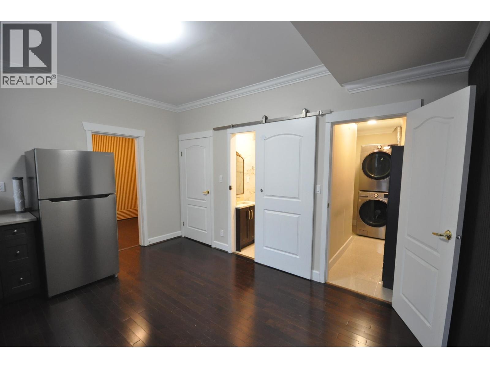 A kitchen with a refrigerator, cabinets, and a washer and dryer in the open closet.