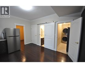 A kitchen with a refrigerator, cabinets, and a washer and dryer in the open closet.