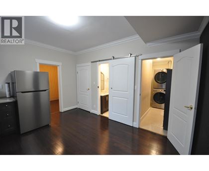 A kitchen with a refrigerator, cabinets, and a washer and dryer in the open closet.
