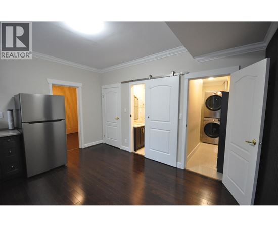 A kitchen with a refrigerator, cabinets, and a washer and dryer in the open closet.