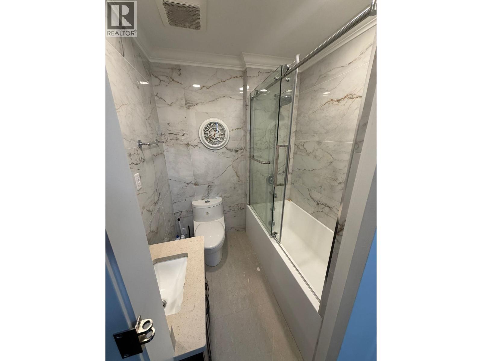 A bathroom with marble walls and a glass shower stall.