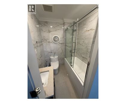 A bathroom with marble walls and a glass shower stall.
