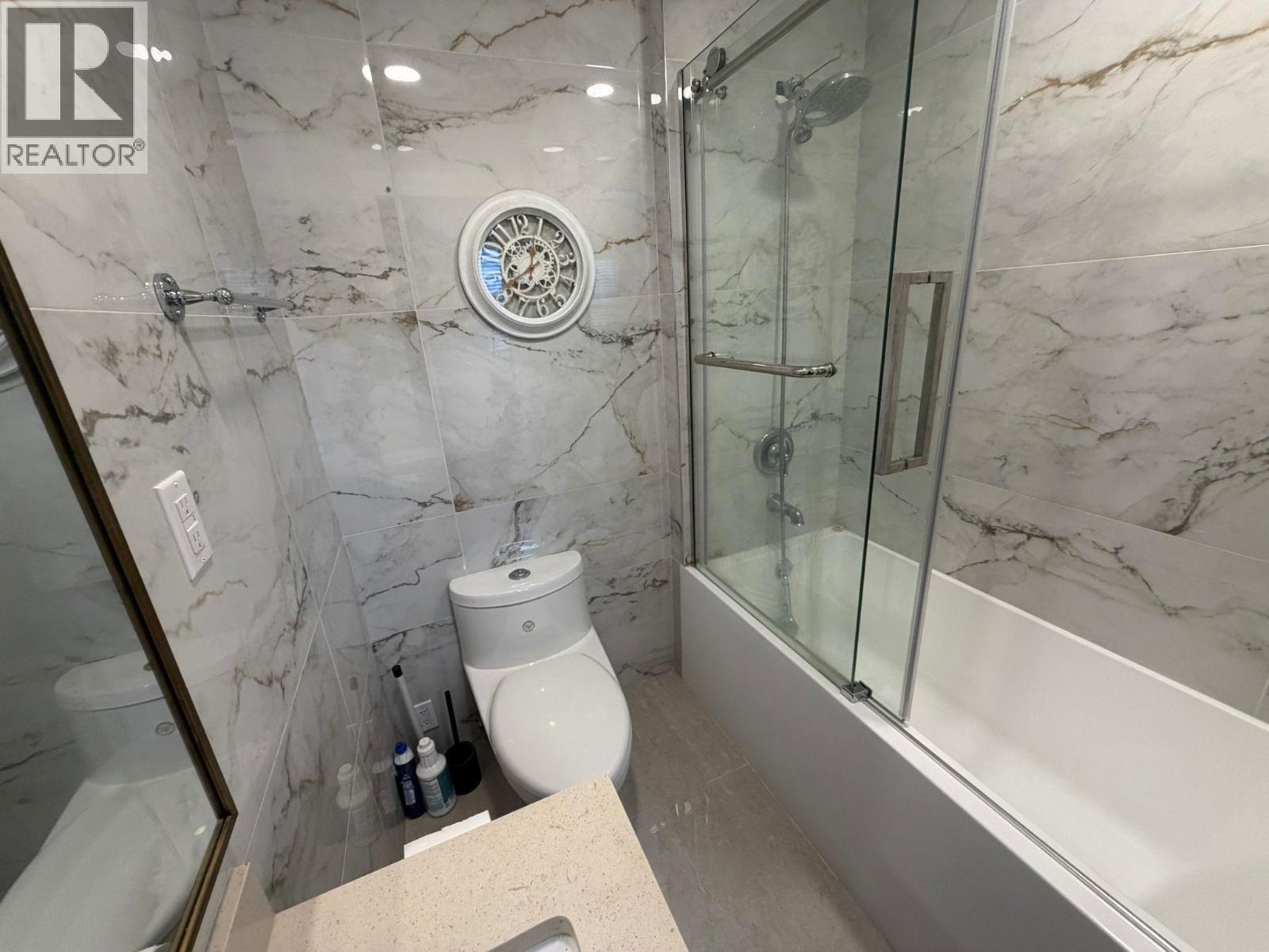 A bathroom with marble walls and a glass shower stall.