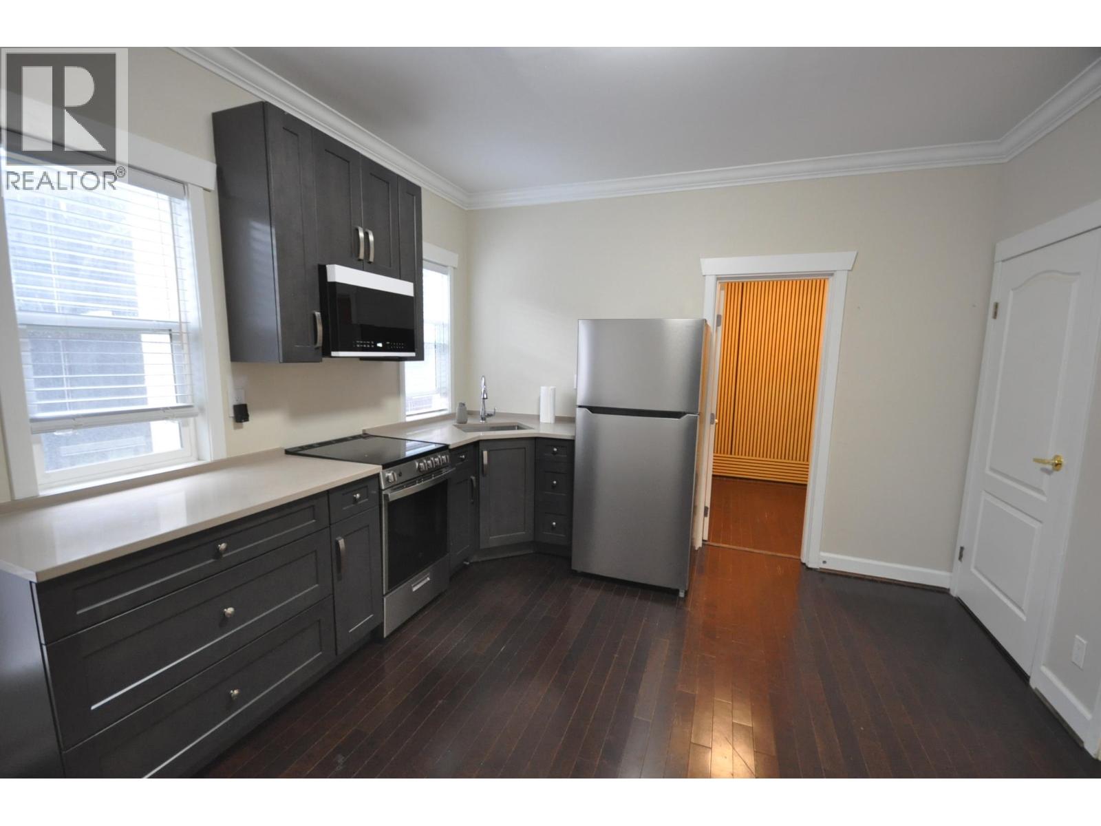 A kitchen with dark wood floors and white walls.