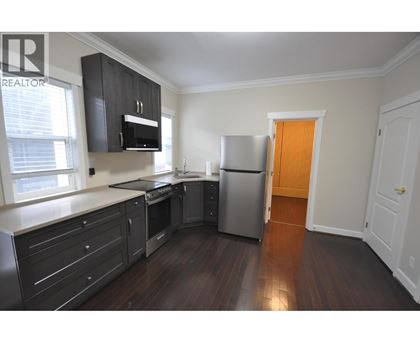 A kitchen with dark wood floors and white walls.