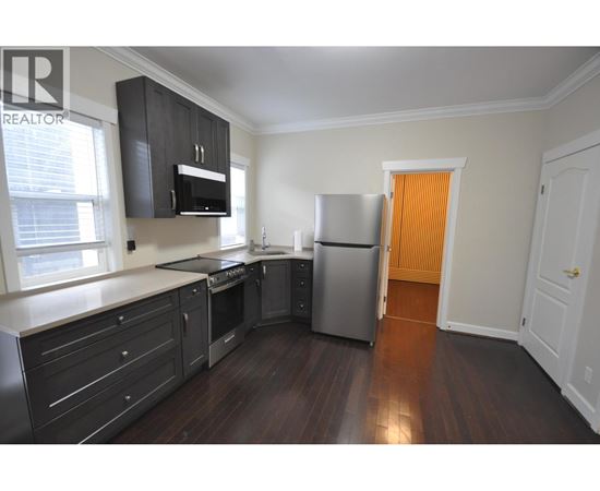 A kitchen with dark wood floors and white walls.