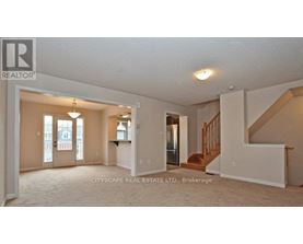A real estate listing photo of a spacious room with a staircase.