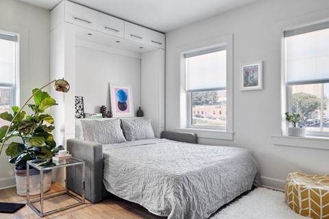 A bedroom with a bed, a plant, and a picture on the wall.