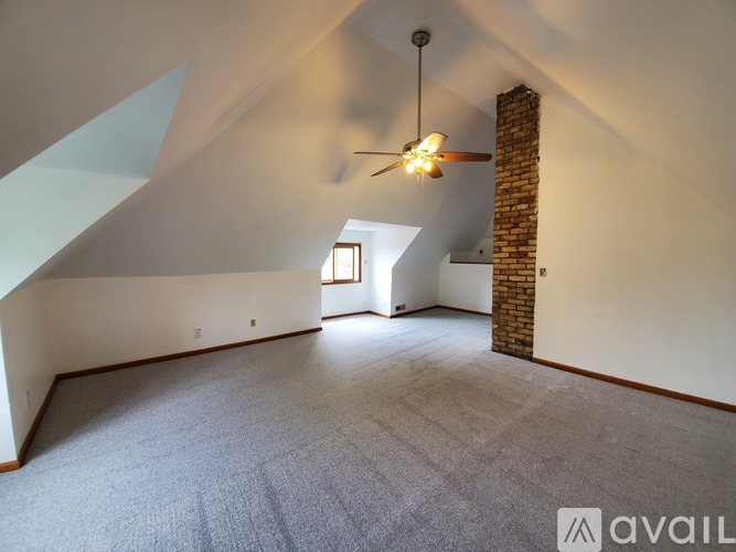 A spacious attic room with a ceiling fan and a window.