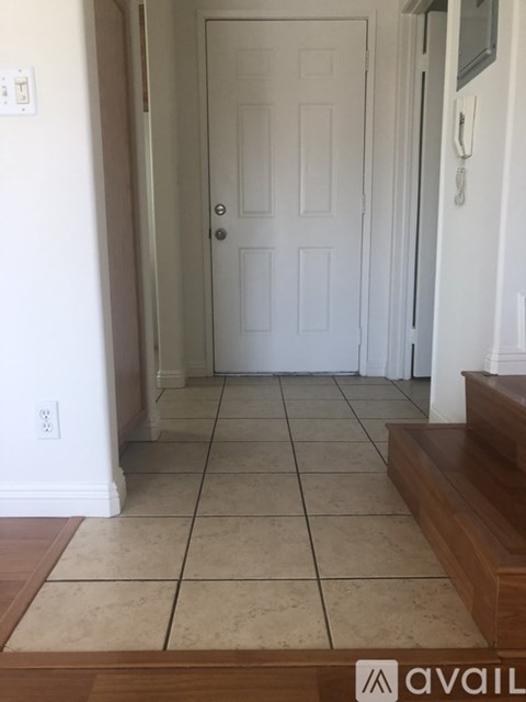 A hallway with a white door and tiled floor.