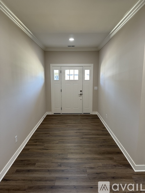 A hallway with wood flooring and white walls leading to a white door.