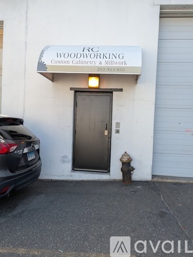 A woodworking shop is located in a white building with a black door.