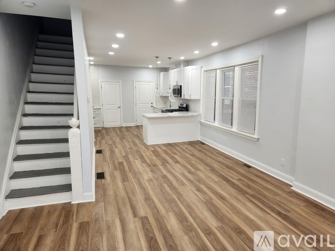 A spacious room with wooden flooring and a staircase on the left side.