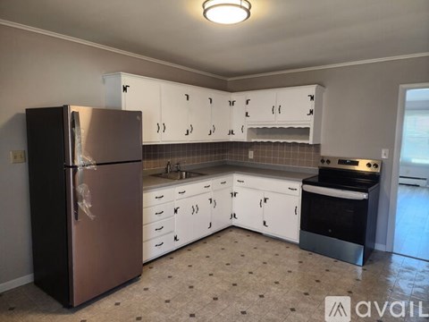 A kitchen with a black fridge, white cabinets, and a tiled backsplash.