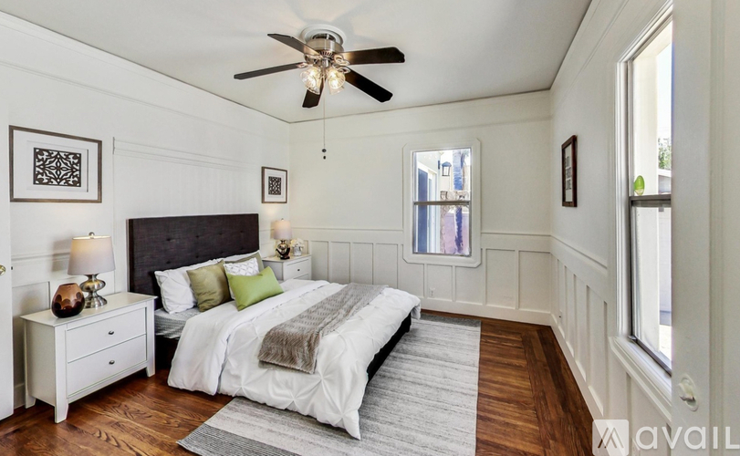 A bedroom with a large bed, a ceiling fan, and a nightstand with a lamp.