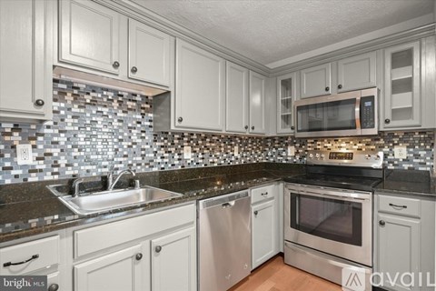 A kitchen with white cabinets and a black counter top.