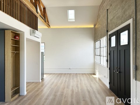 A spacious room with wooden floors and a black door on the right.