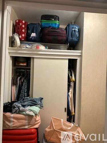 A closet with a white shelf holding luggage and a red chair.