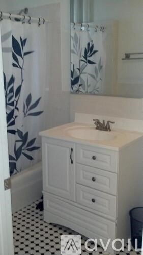 A white bathroom vanity with a marble countertop and a shower curtain with leaf patterns.