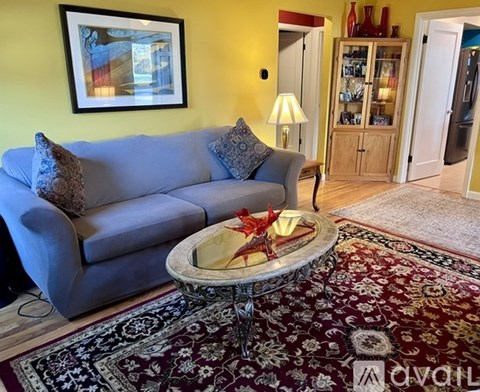 A living room with a grey couch, a round table with a glass top, and a rug.