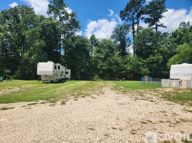 A white RV is parked in a gravel lot surrounded by trees.