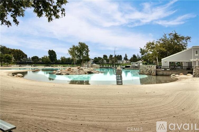 A sandy area with a pool and a building in the background.