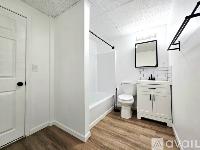 A white bathroom with wood flooring and a white door.