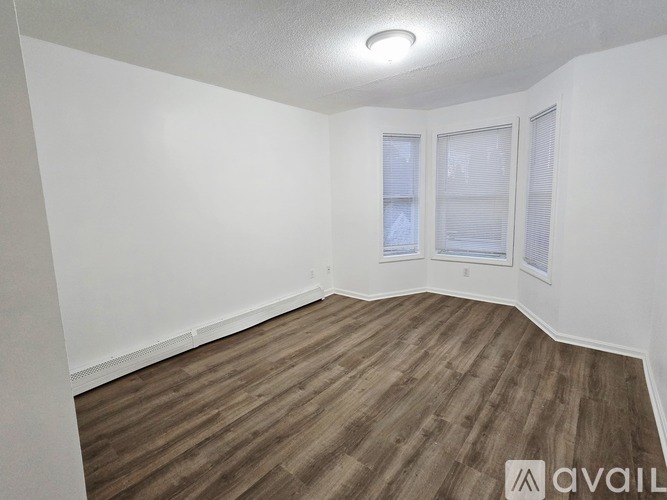 A room with wooden flooring and three windows.